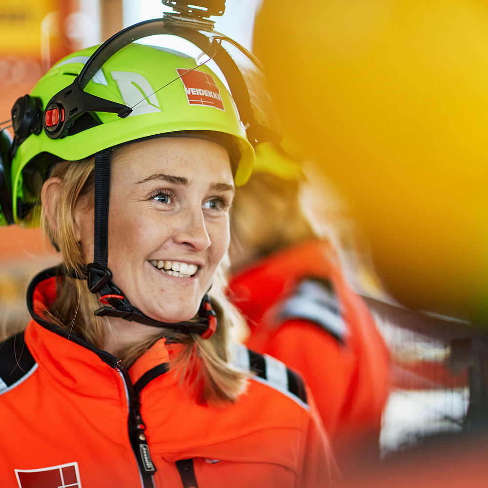 Kvinne på byggeplass, smilende ser til siden.