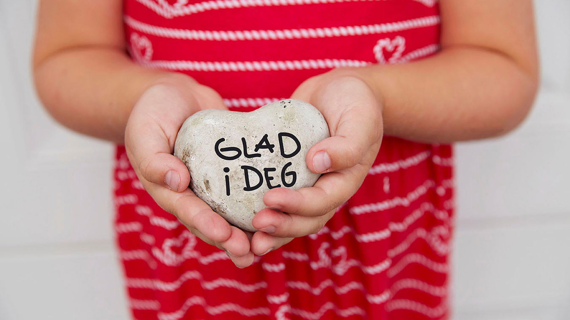 Barn holder stein formet som hjerte med "glad i deg" skrevet inn. Foto.