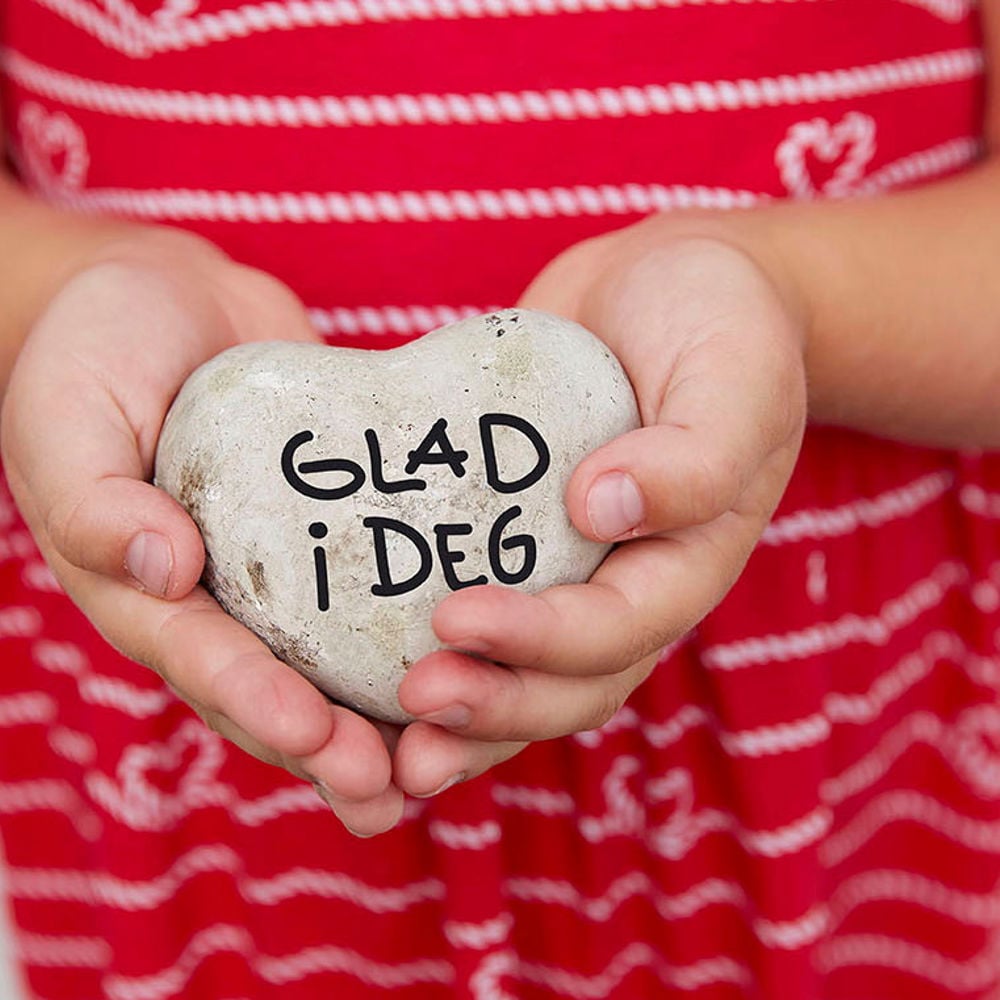 Barn holder stein formet som hjerte med "glad i deg" skrevet inn. Foto.