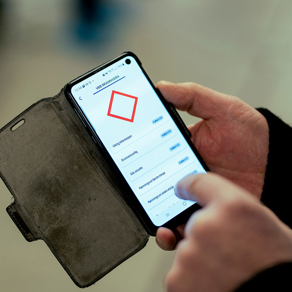 Mann holder telefon og trykker. Foto.