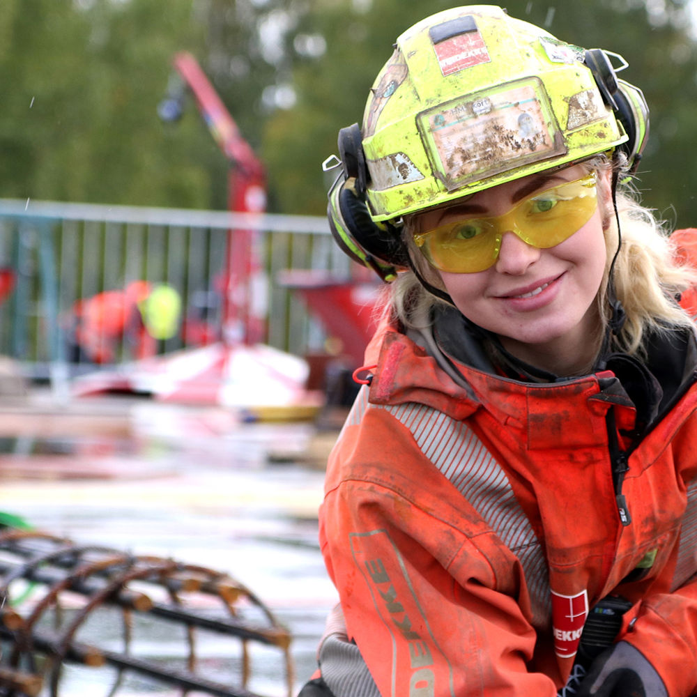 Kvinne på byggplass jobber med betong. Foto.