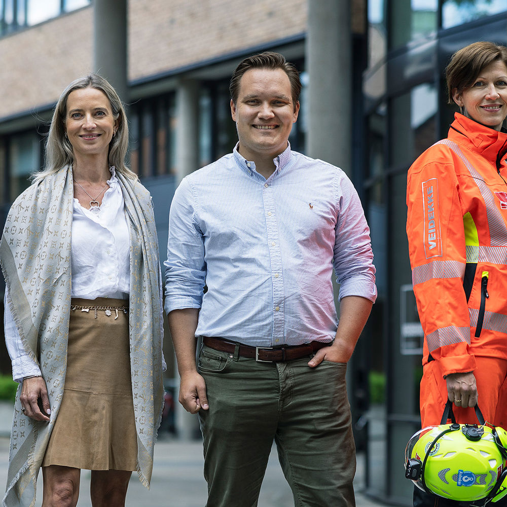Smilende personer på byggeplass med hjelm og briller. Foto. 
