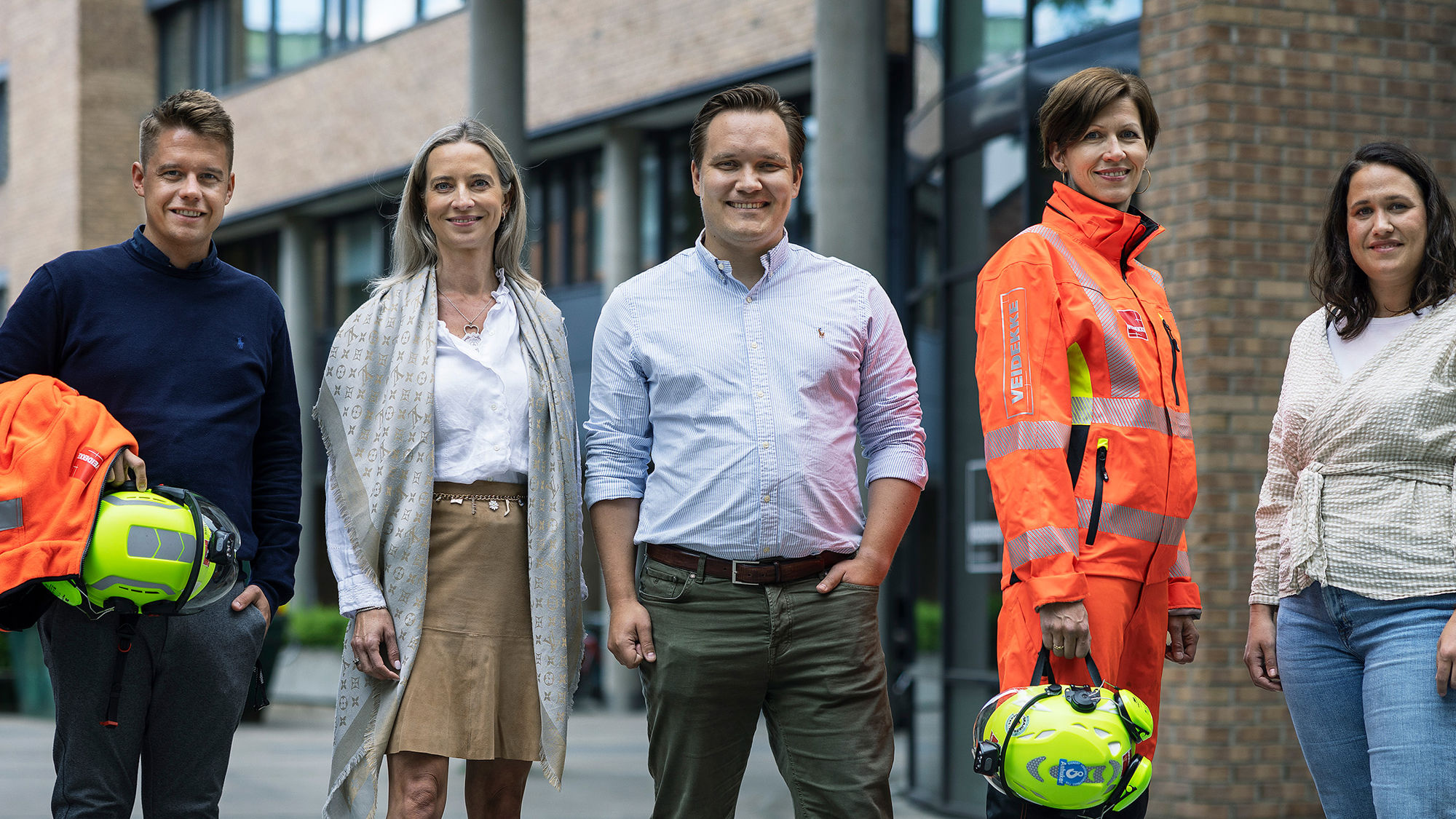 Smilende personer på byggeplass med hjelm og briller. Foto. 