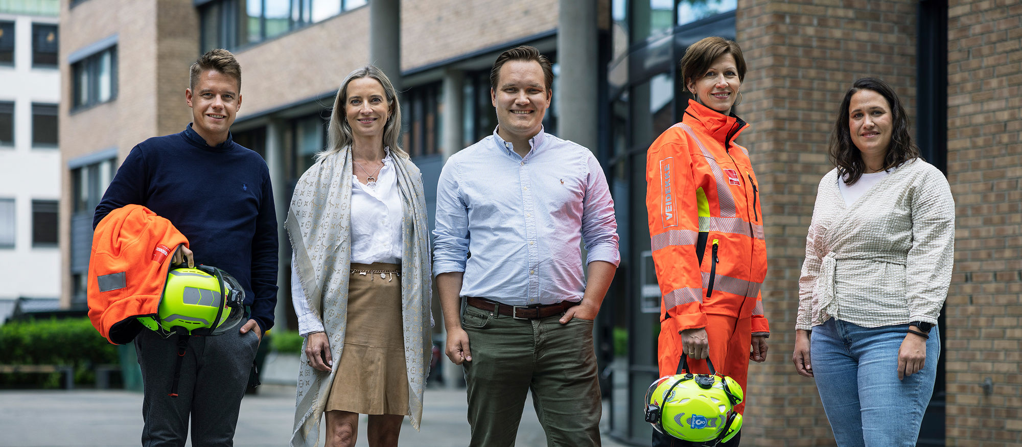 Smilende personer på byggeplass med hjelm og briller. Foto. 