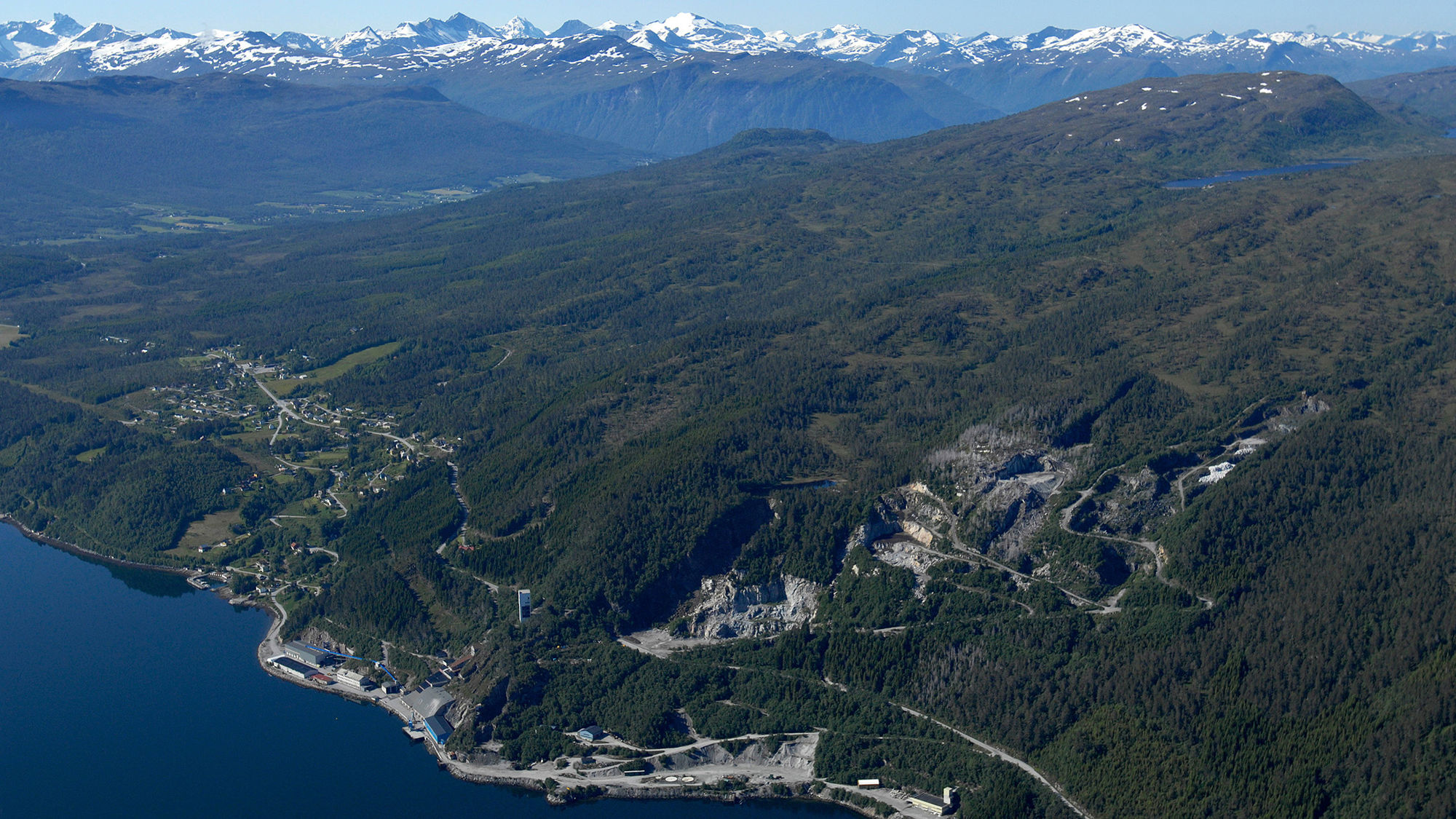 Flyfoto med utsikt over fjord og fjell. Massemottak i åsside. Foto.