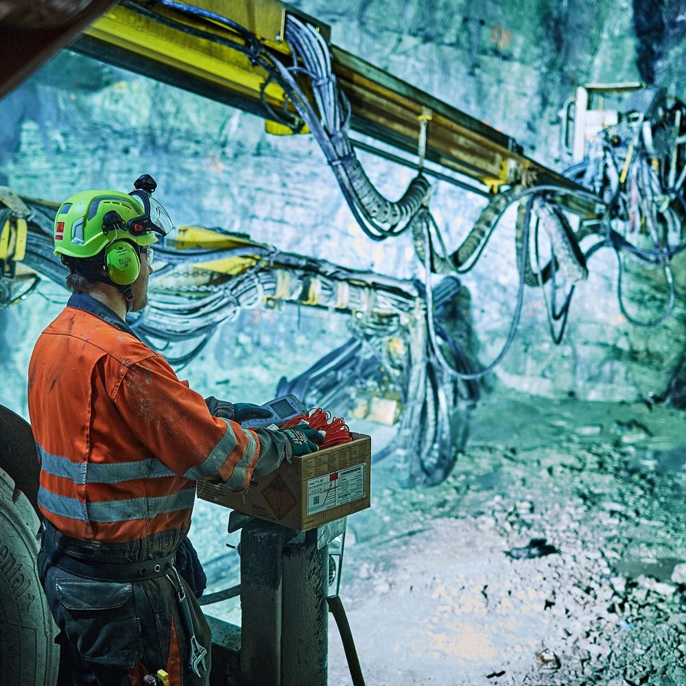 Mann på borerigg i tunnel, setter ladning for sprenging. Foto.